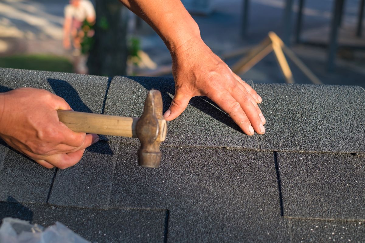 Workers hands installing bitumen roof shingles using hammer, St Paul